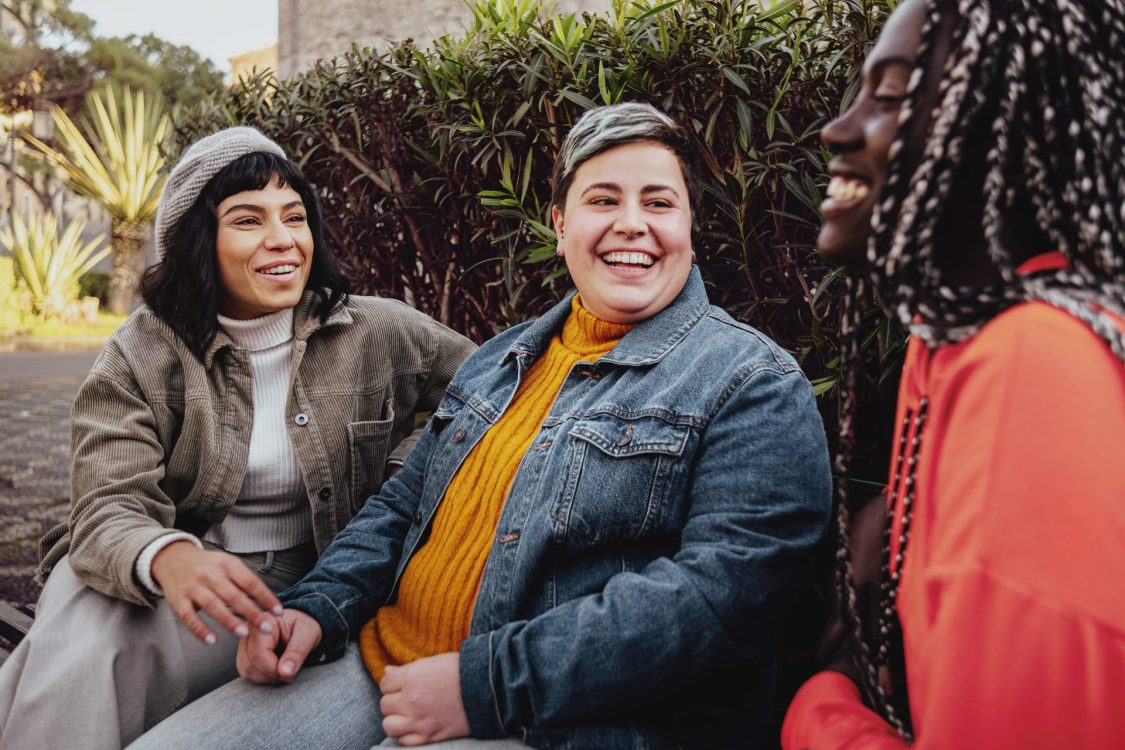 Interracial cheerful group of happy girls having fun talking together in the park talking and having fun sitting on a bench in the park Vacatures 7